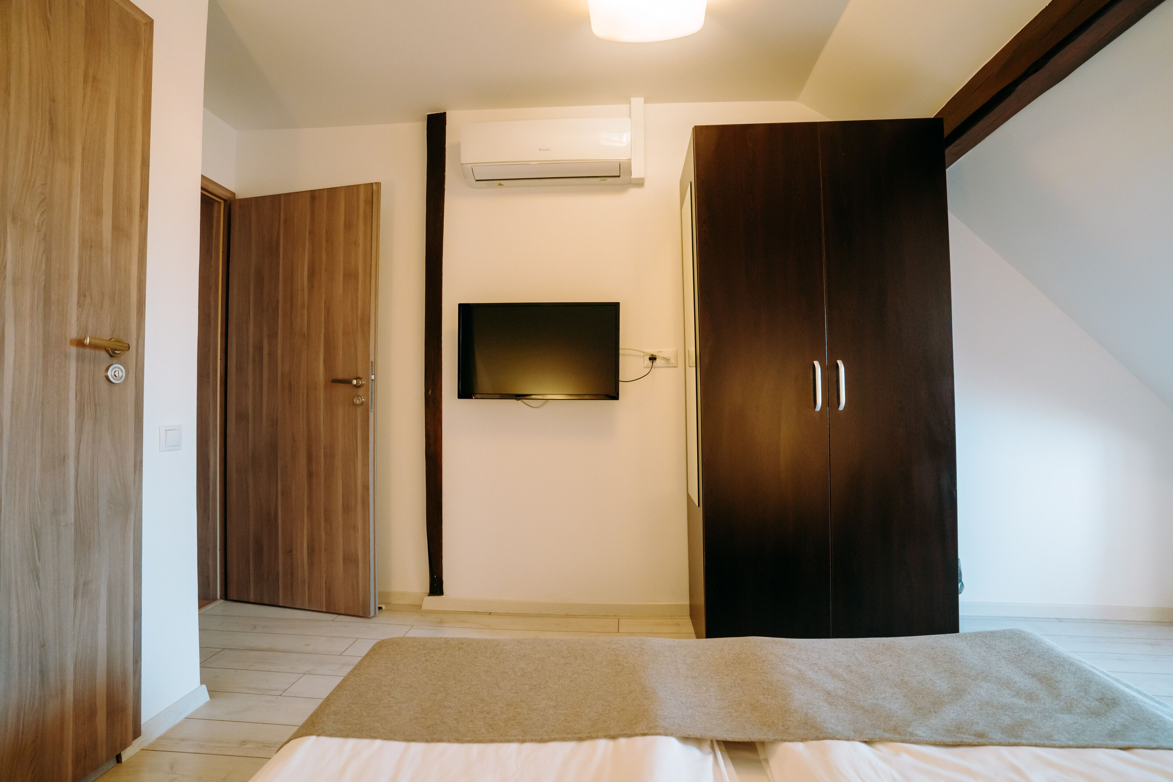 Een slaapkamer met een bed, een houten kledingkast, een flatscreen televisie aan de muur en een airconditioningsysteem.
