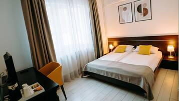 Quarto de hotel com uma cama, uma escrivaninha, uma cadeira e uma televisão.