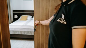 A person holding a key near a wooden door, with a bed and a nightstand visible in the background. - Vila Anca (Sibiu)