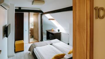A bedroom with a bed, a small table, a plant, and a window.