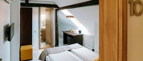 A bedroom with a bed, a small table, a plant, and a window.
