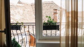 Vista a través de una ventana con barandilla de metal, tejado de baldosas y algo de vegetación.