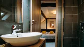 Ein modernes Badezimmer mit einem großen, weißen Waschbecken, einer Dusche und einem Bett mit gelben Kissen.
