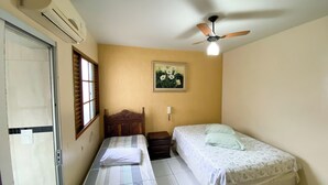 A bedroom with two beds, a ceiling fan, a window with blinds, and a wall-mounted air conditioner.