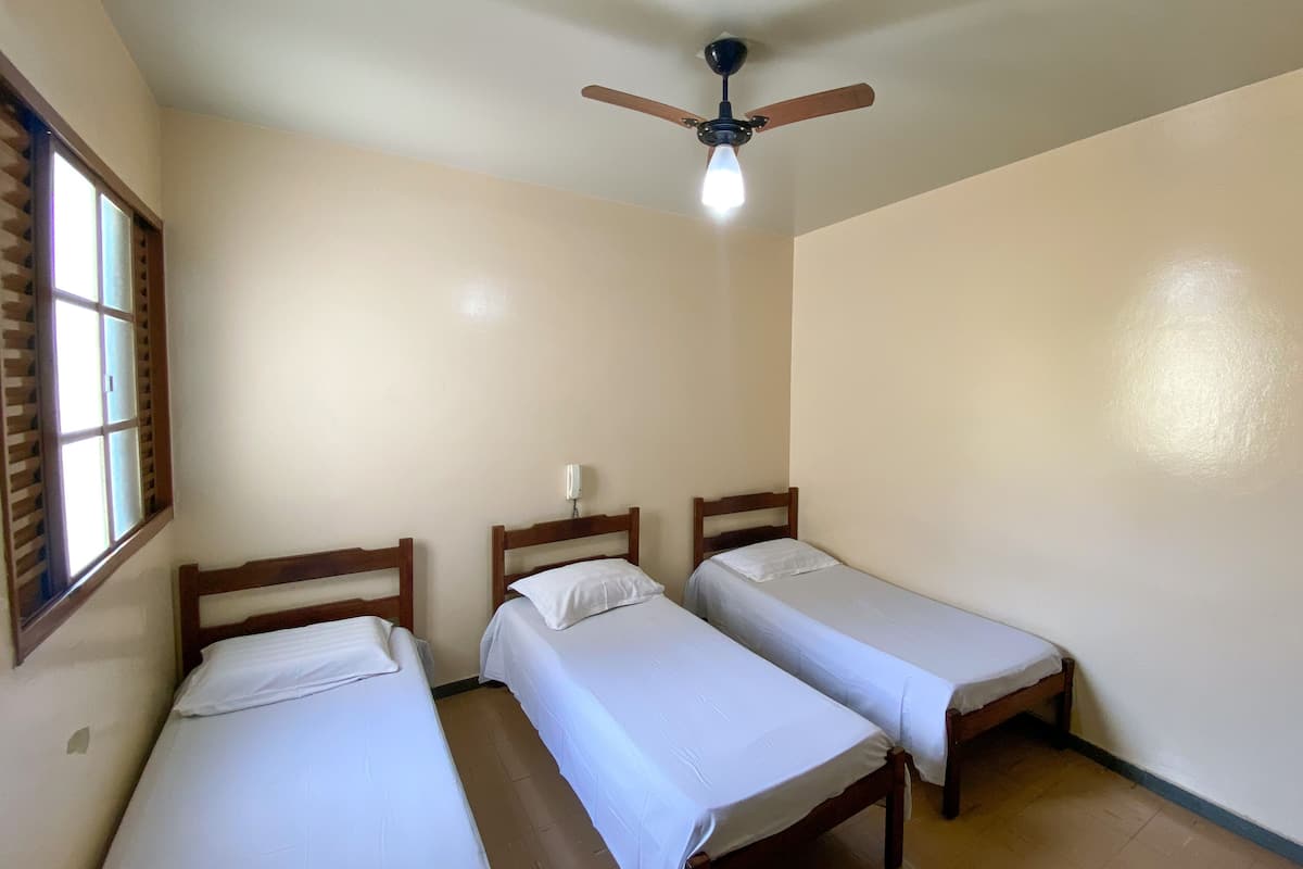 A room with three single beds, a ceiling fan, and a window with blinds.