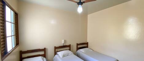 A room with three single beds, a ceiling fan, and a window with blinds.