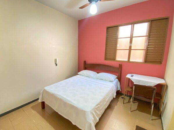 Un dormitorio con cama, escritorio, silla, ventilador de techo y ventana con persianas.