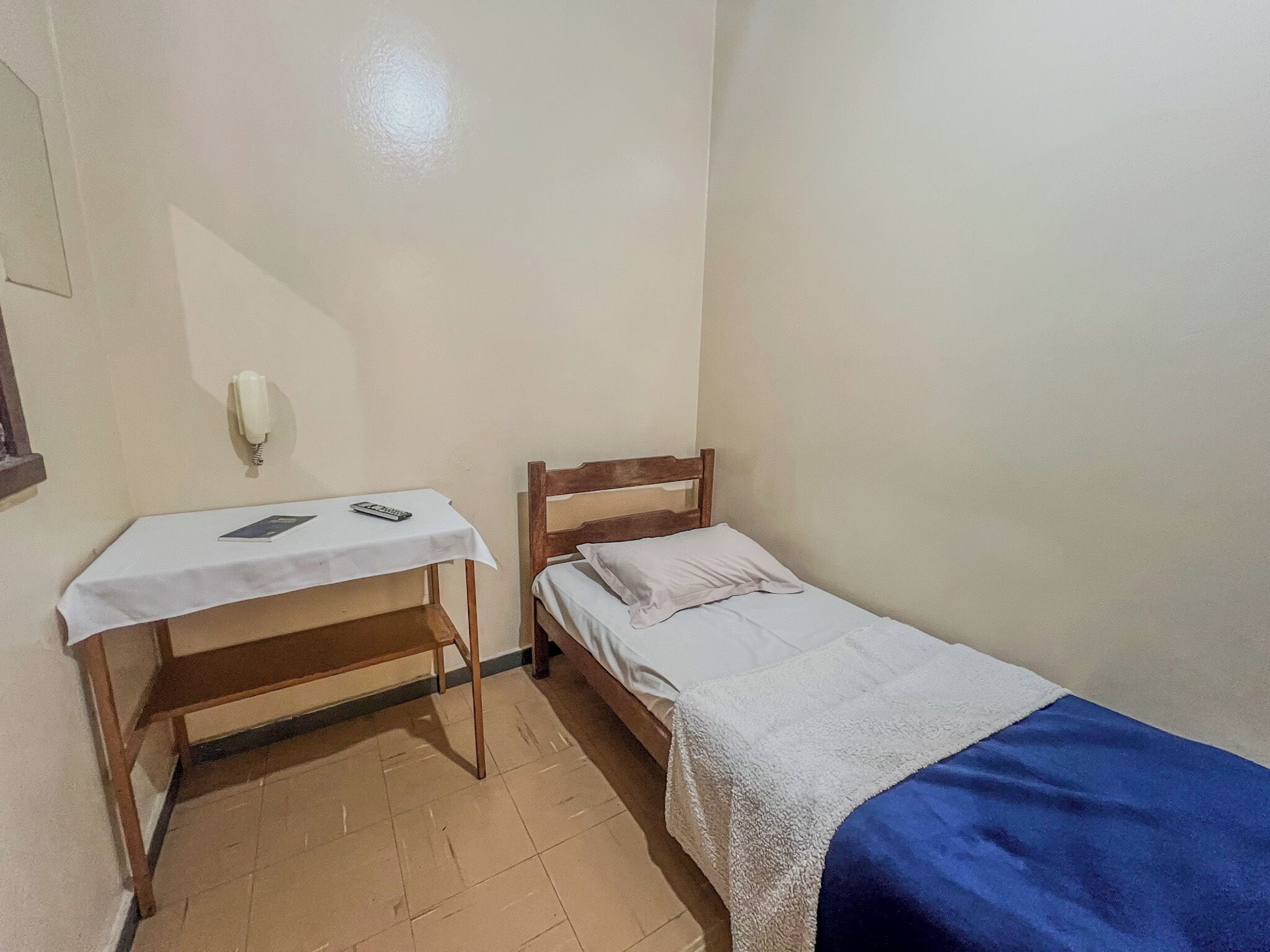 Una stanza modesta con un letto, un comodino e una scrivania con una sedia.