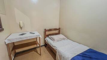 Una stanza modesta con un letto, un comodino e una scrivania con una sedia.