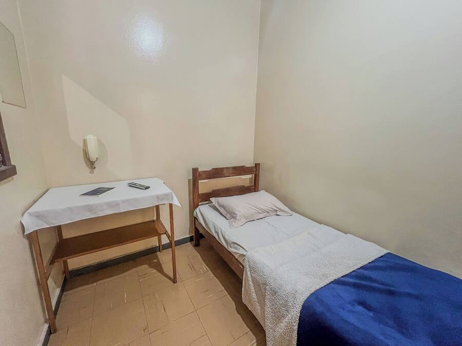 Una stanza modesta con un letto, un comodino e una scrivania con una sedia.
