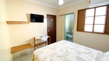 Un dormitorio con una cama, un escritorio, una silla, un televisor, una puerta y una ventana.