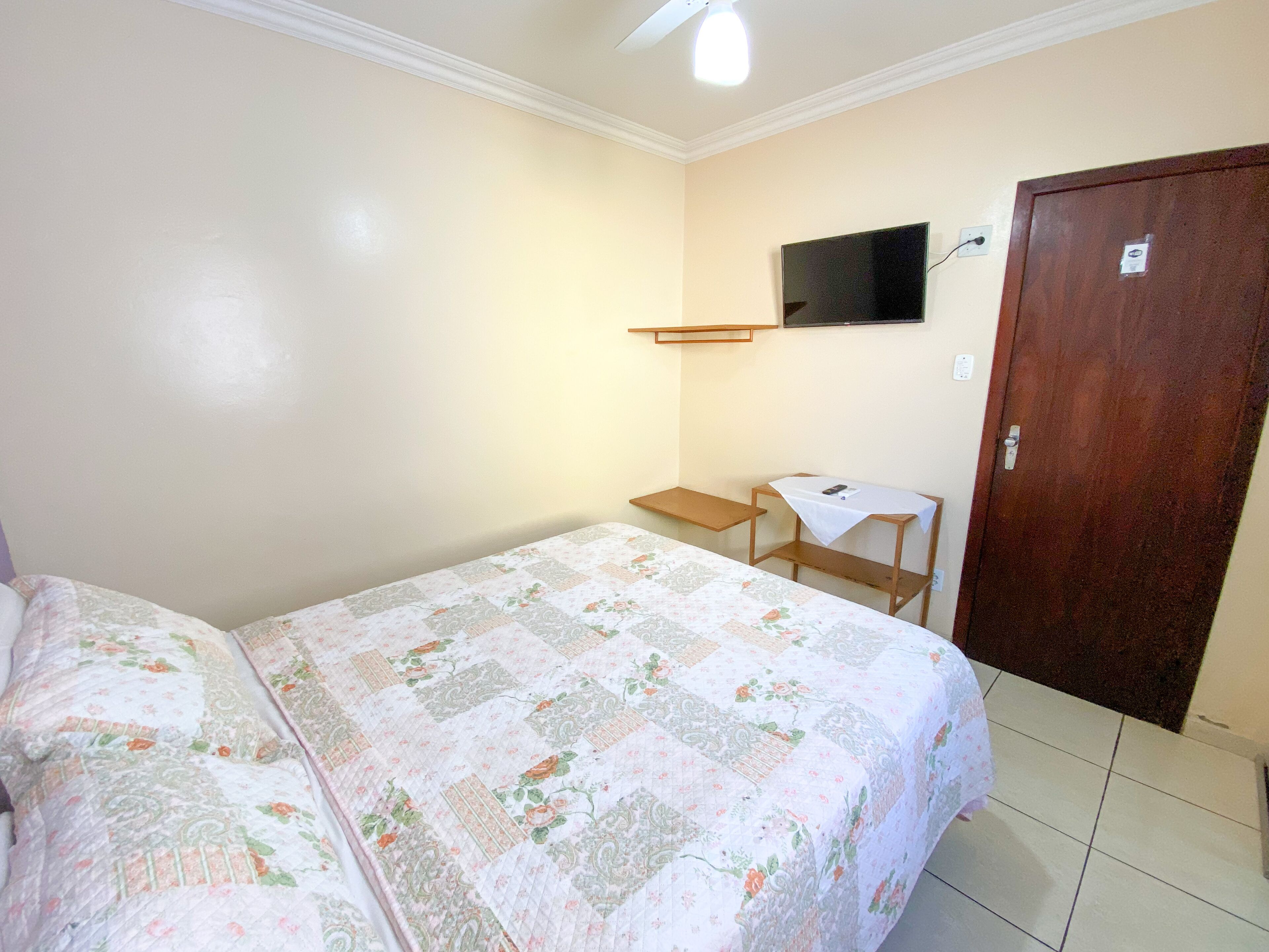 A small, clean room with a bed, a desk, and a TV mounted on the wall.