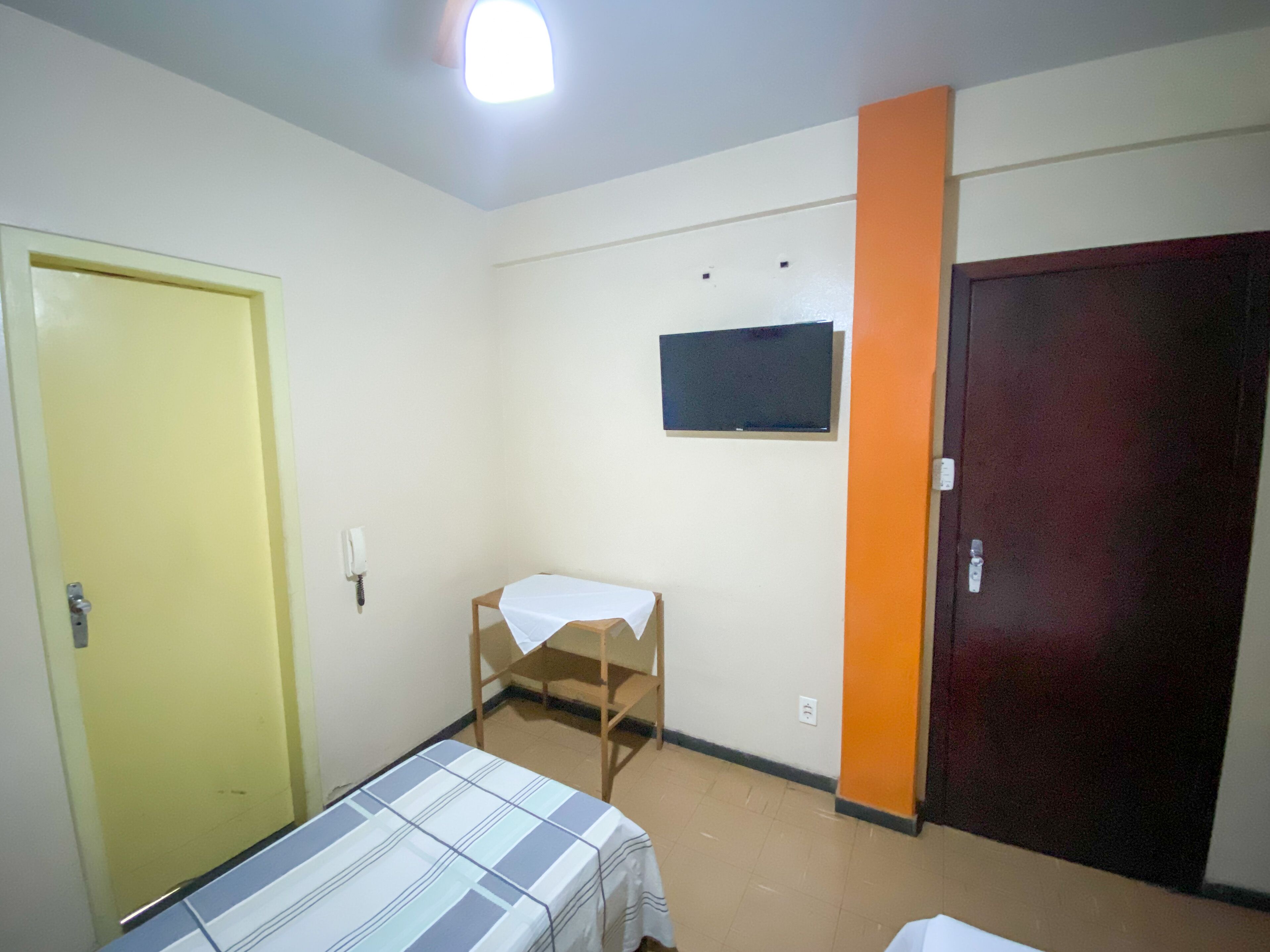 Una habitación con cama, escritorio, televisor y puerta.