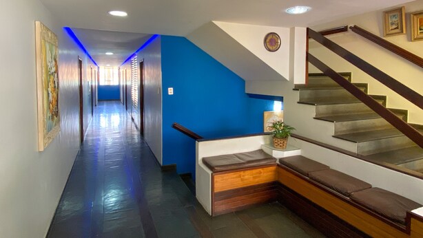 A hotel hallway with a blue accent wall, a staircase, and a bench.