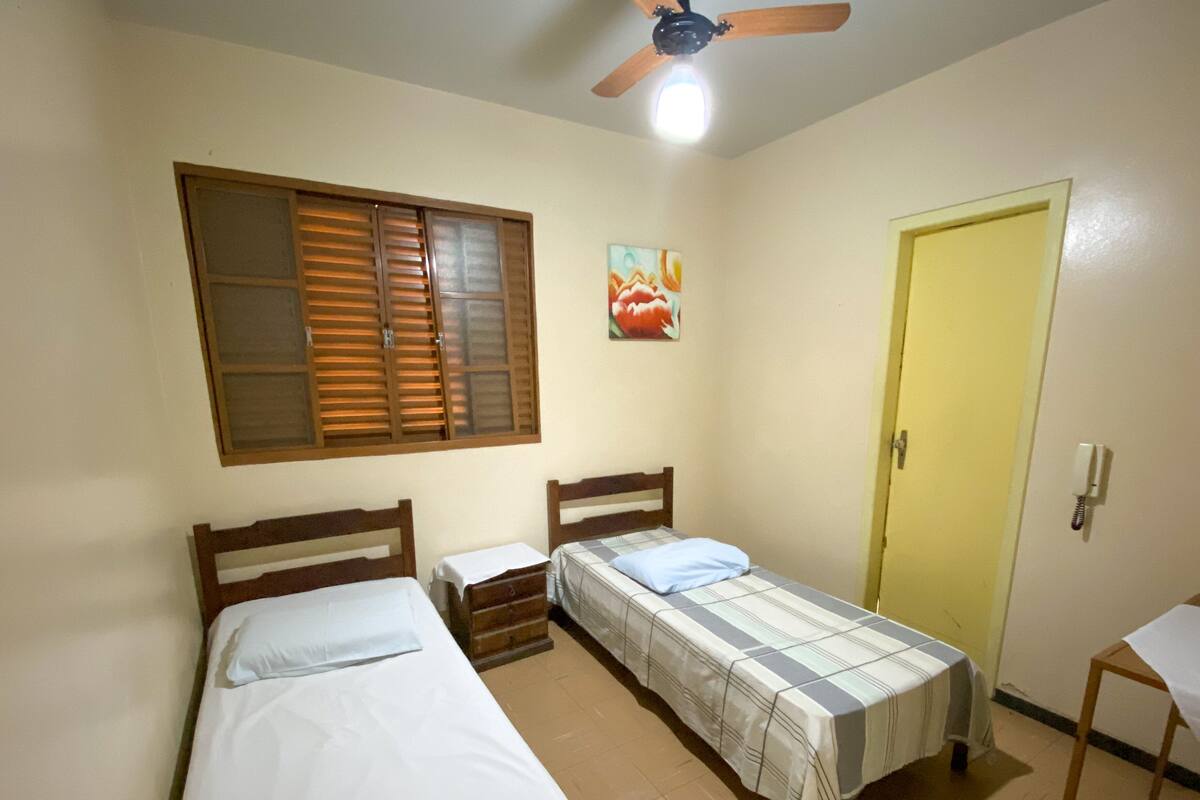 A room with two single beds, a wooden headboard, a small table, a yellow door, and a ceiling fan.