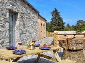 Une terrasse en bois avec une table dressée pour un repas, un bâtiment en pierre et une clôture en bois.