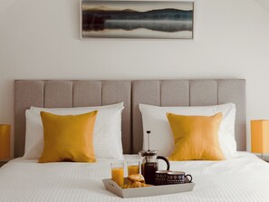 Een hotelkamer met een bed, twee kussens, een koffiezetapparaat en een dienblad met croissants en sap.