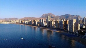 A coastal cityscape with high-rise buildings, a marina, and mountains in the background.