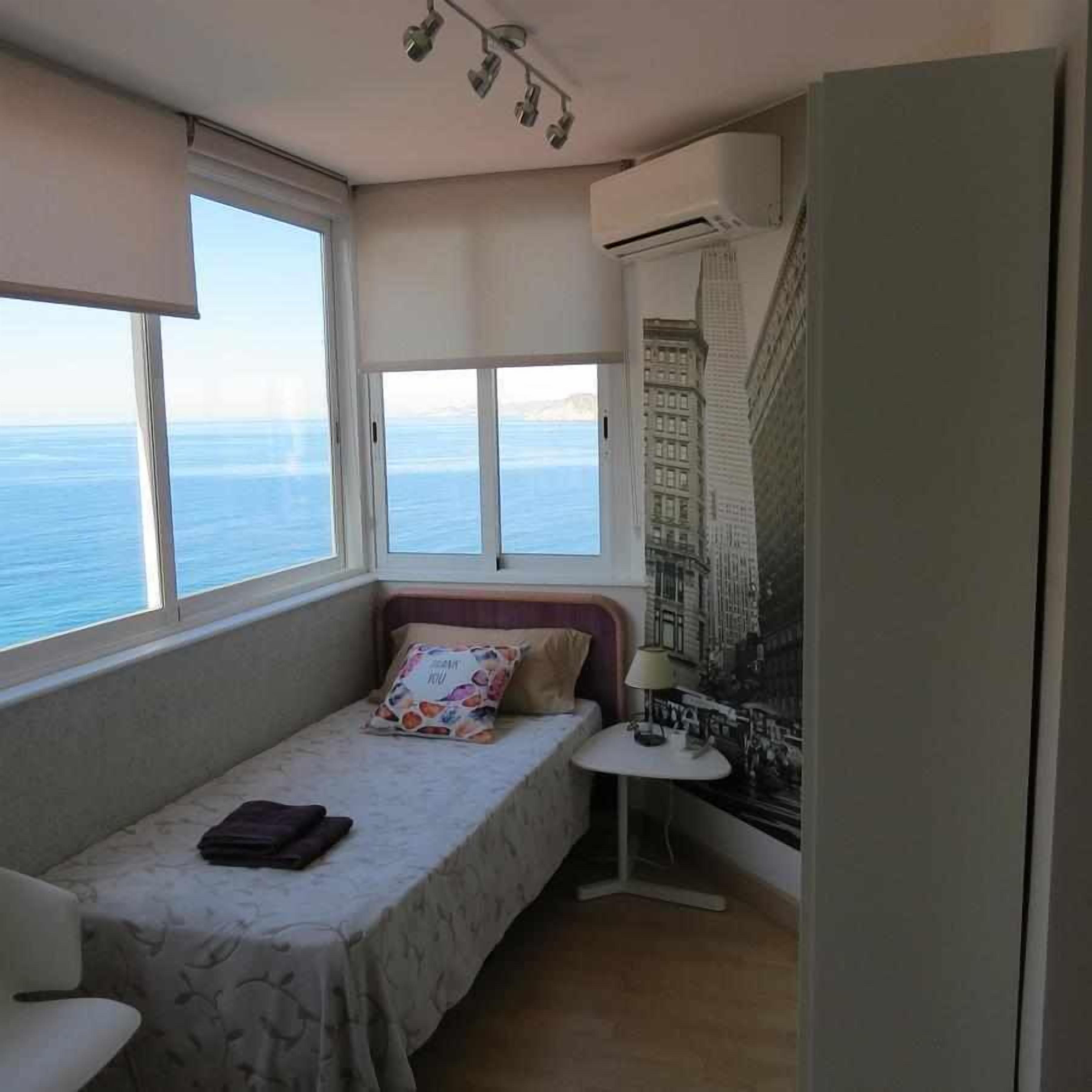 Une petite pièce, de taille modeste, comprenant un lit, une chaise, une table et une fenêtre donnant sur la mer.