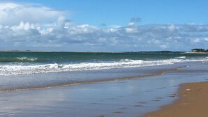 Ein Strand mit Wellen, einem klaren Himmel und einem fernen Leuchtturm.