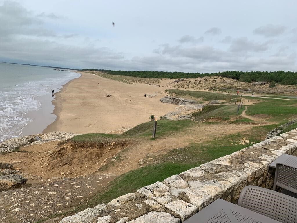 A beach with a stone wall in the foreground and a grassy area with a path leading to the water.