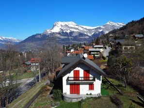 A white building with red shutters, a balcony, and a view of snow-capped mountains.