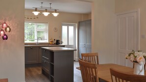 Een keuken met een centraal eiland, houten stoelen, een eettafel en een klok aan de muur.
