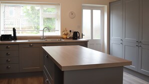 Een keuken met een centraal eiland, een raam met zonwering, een spoelbak en kasten.