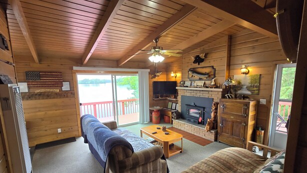 A cozy cabin interior with a fireplace, wooden furniture, and a view of a lake through large sliding doors.