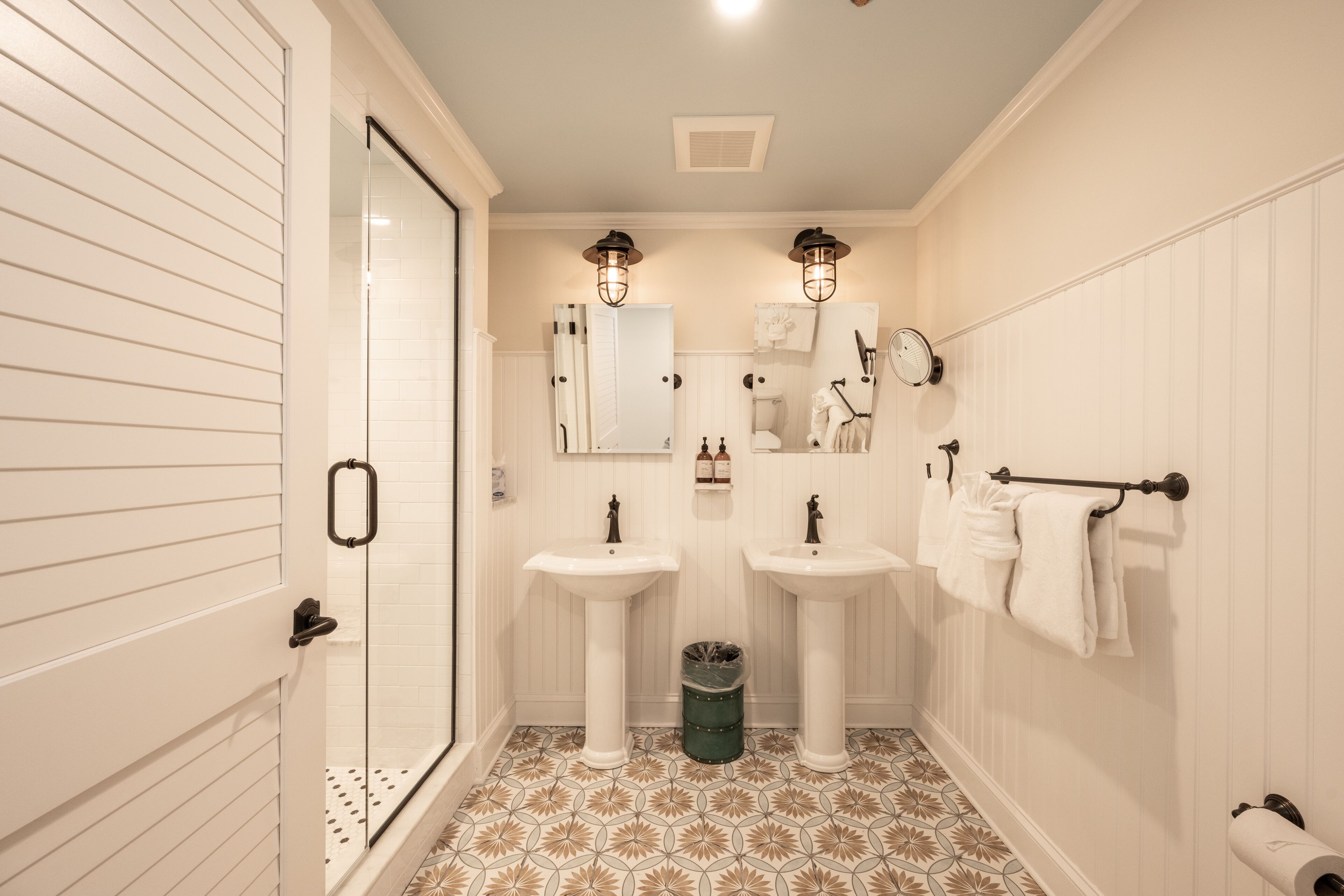 Un baño con dos lavamanos, cabina de ducha de vidrio, inodoro y toallero.