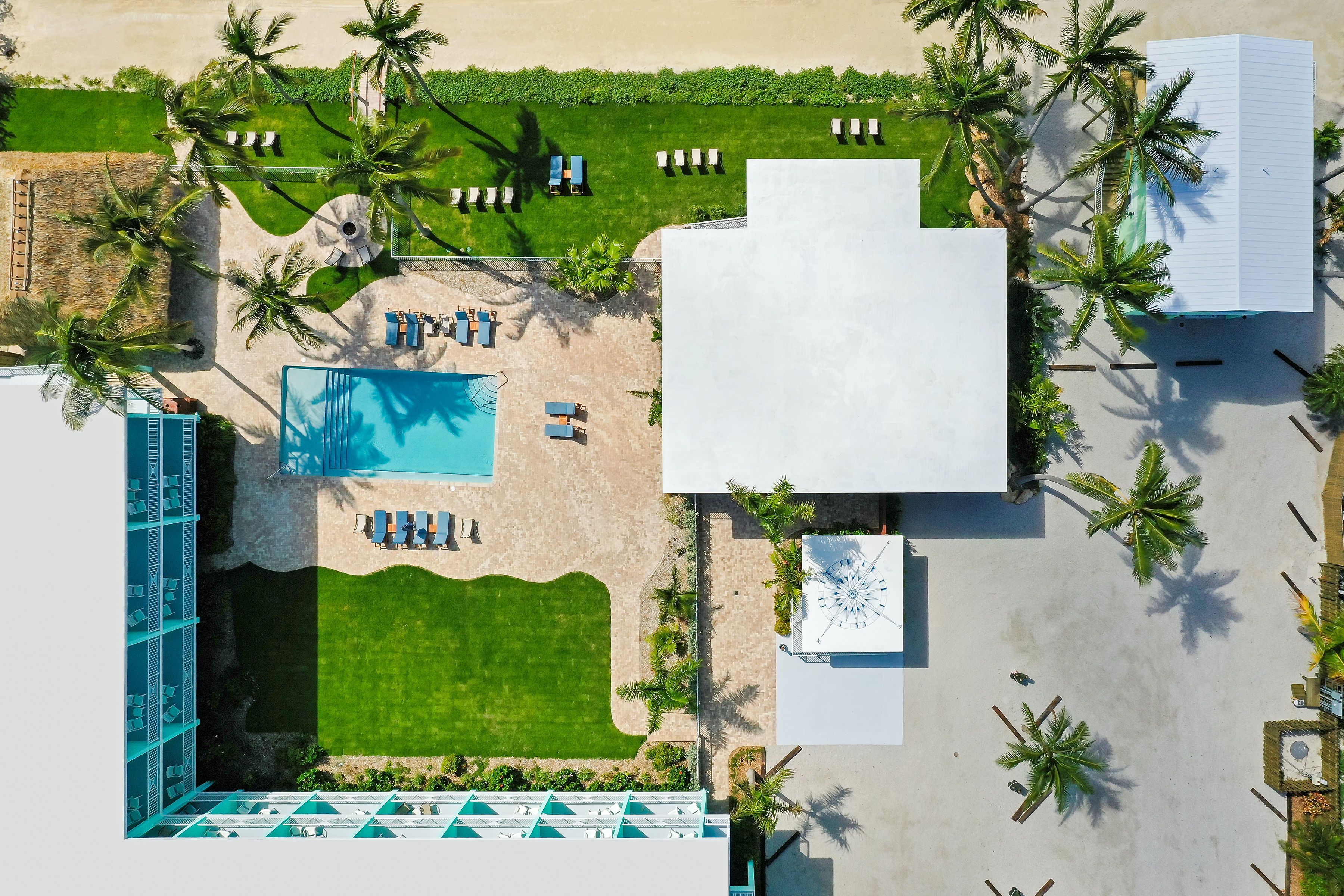 An aerial view of a resort with a swimming pool, sun loungers, and palm trees.