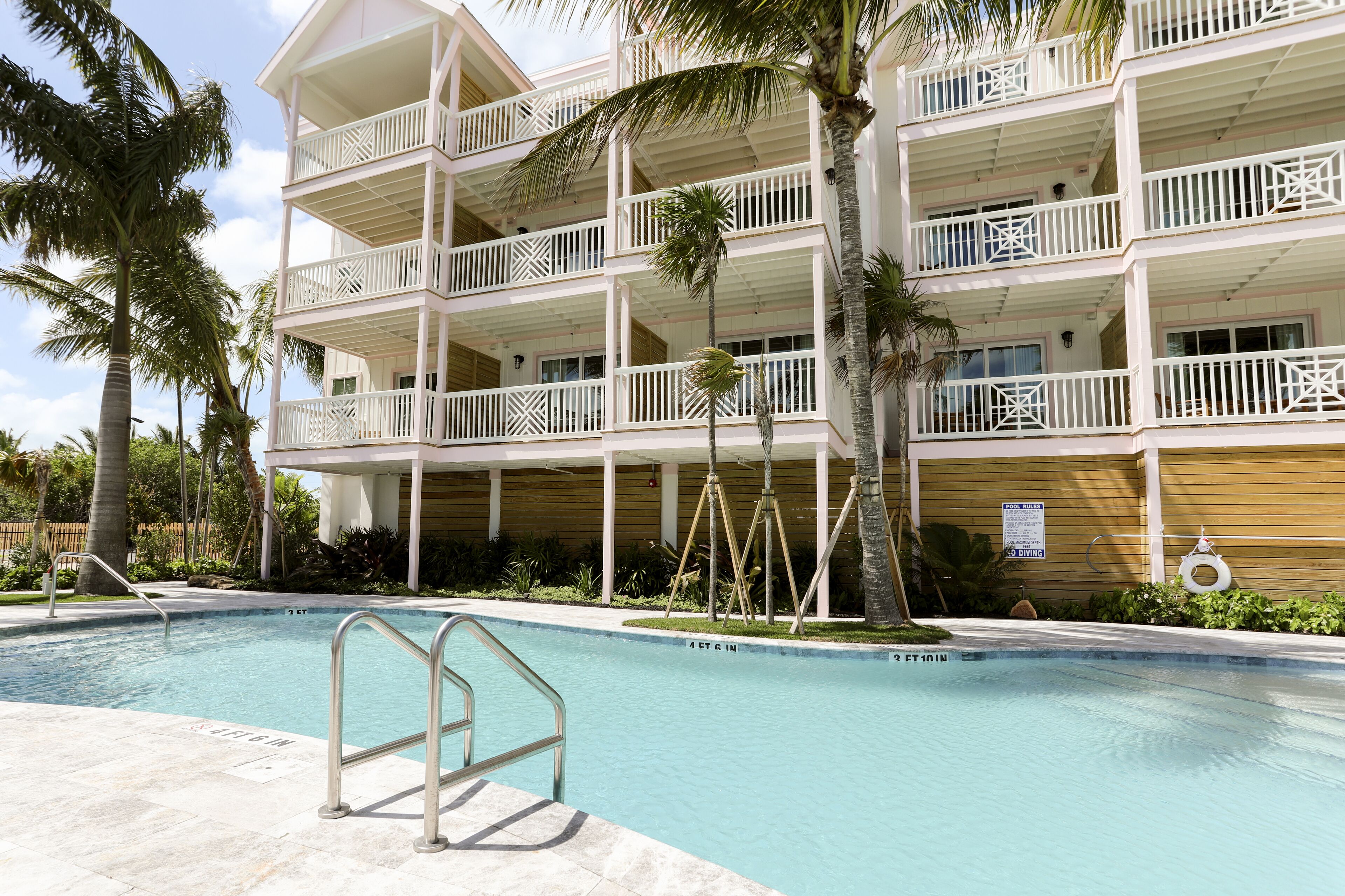 Un hotel de varios pisos con balcones, piscina y palmeras.