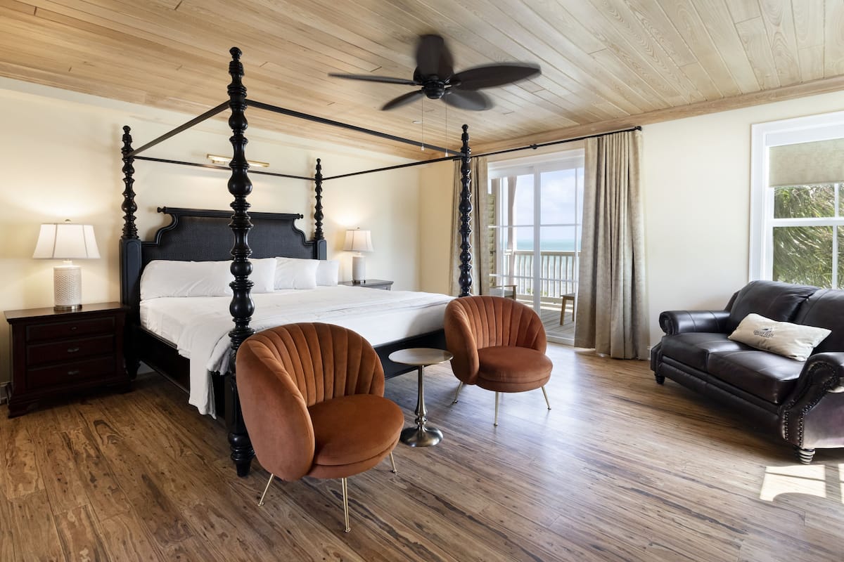 A four-poster bed with a ceiling fan, a dark brown leather sofa, and a small round table with two chairs.