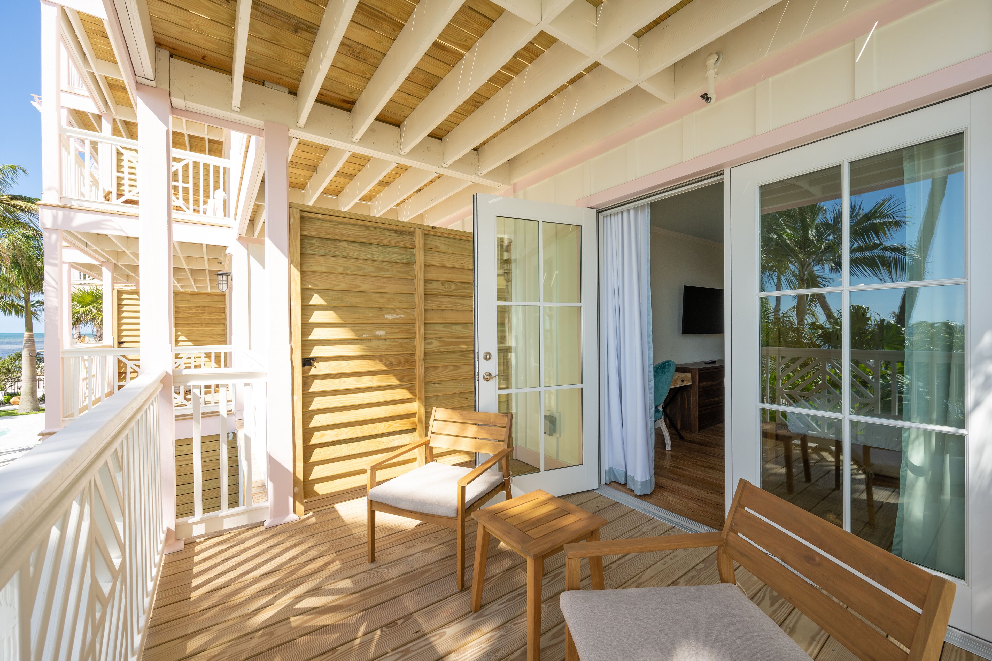 A wooden deck with a glass door leading to a balcony, wooden furniture, and a view of the outdoors.