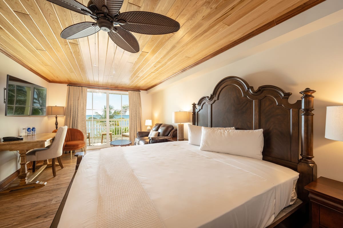 A hotel room with a large bed, wooden ceiling, a desk with a chair, a sofa, and a view of the outdoors.