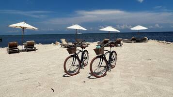 Uma praia com cadeiras de praia e guarda-sóis, uma bicicleta e vista para o oceano.