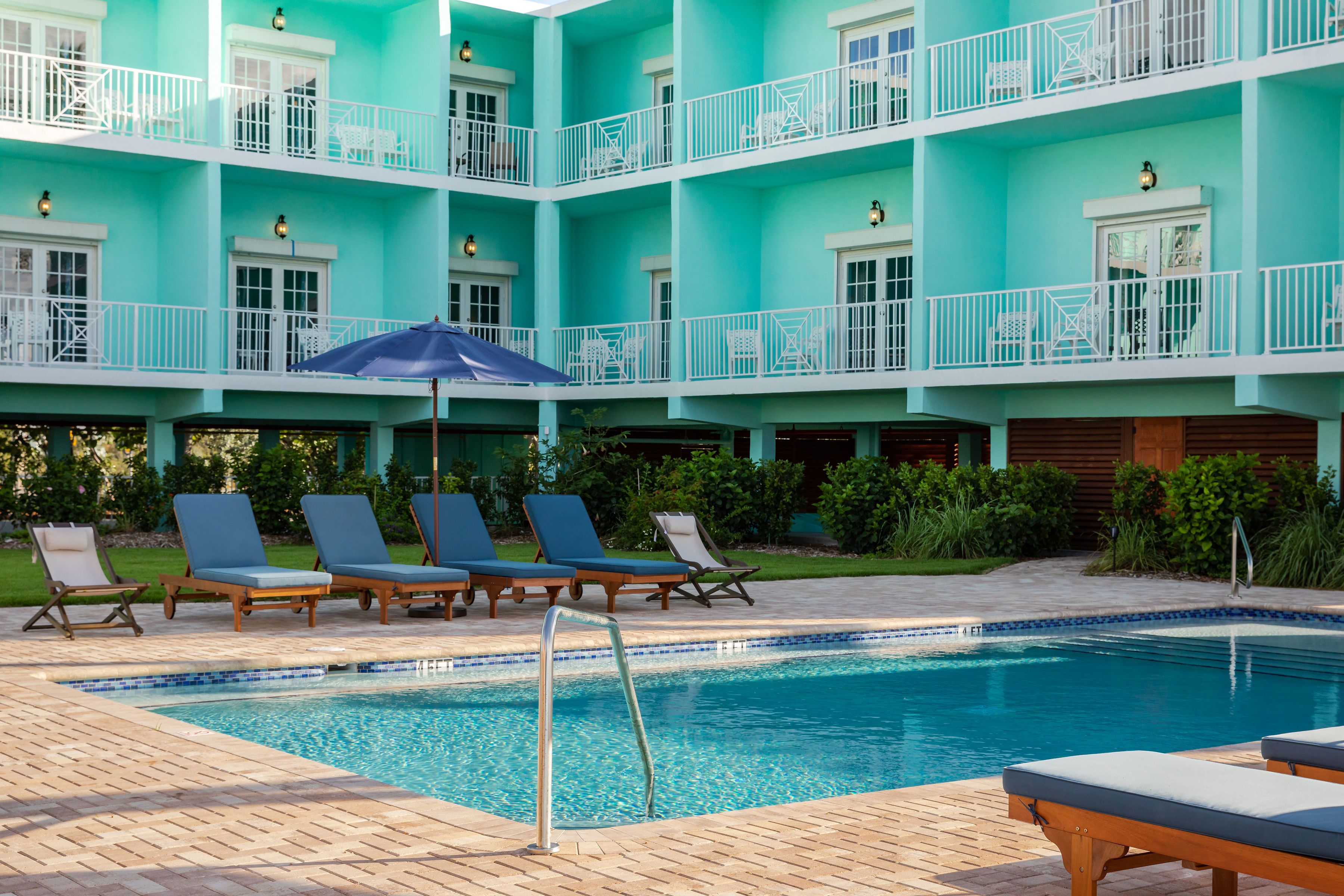 Un hôtel à plusieurs étages, à la façade turquoise, doté d’une piscine et de chaises longues.