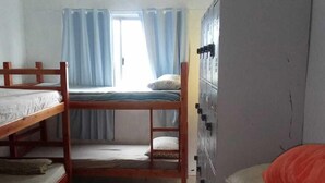 Quarto em dormitório com beliches, guarda-roupa e janela com cortinas.