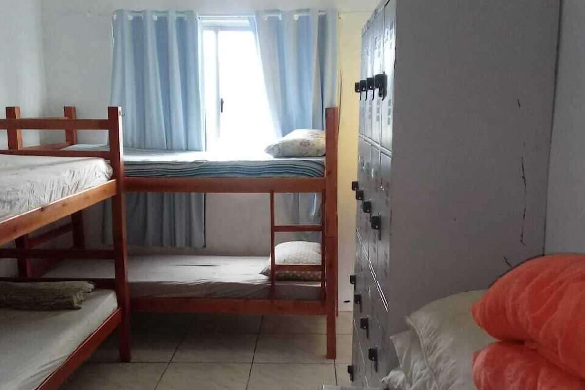 Quarto em dormitório com beliches, guarda-roupa e janela com cortinas.