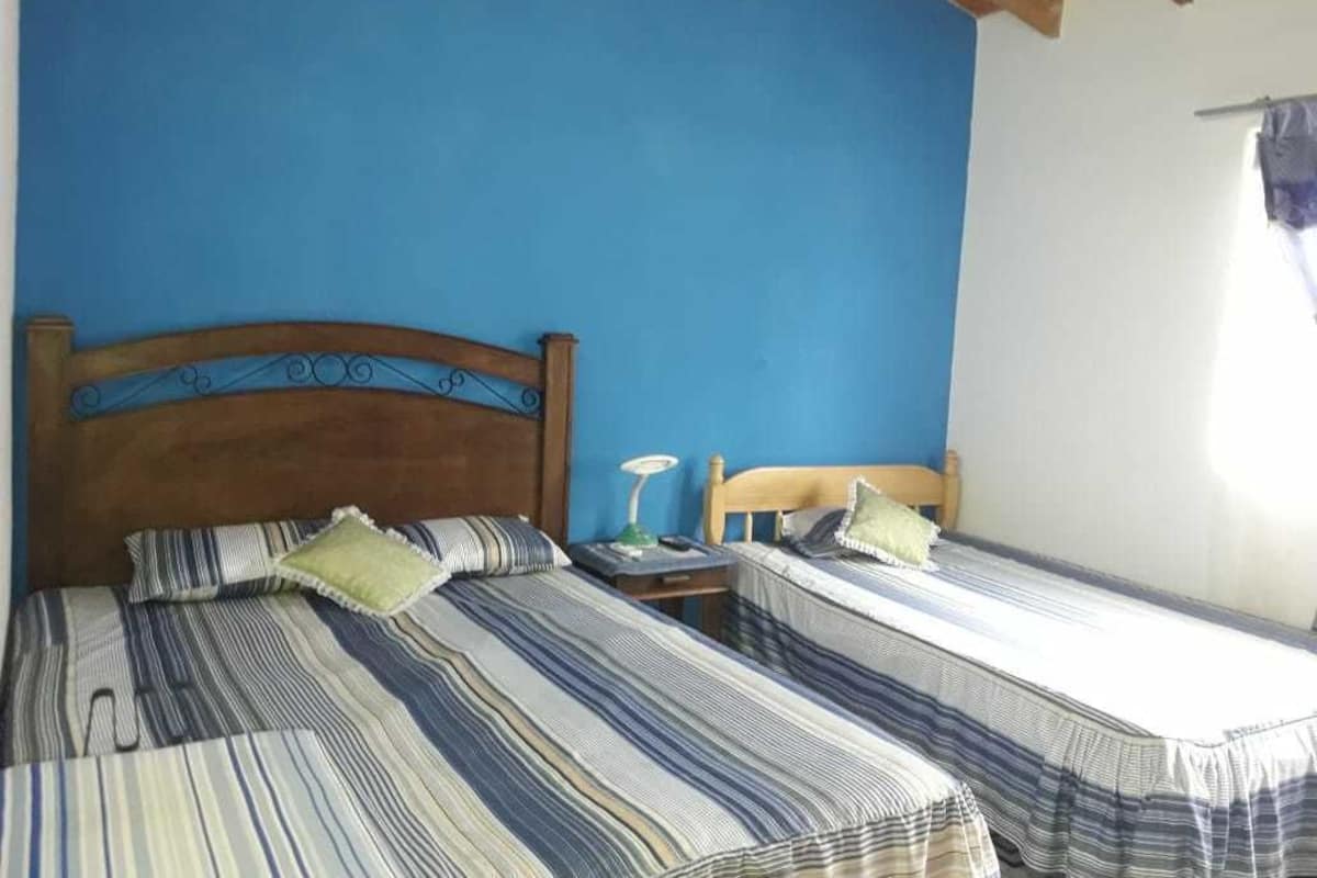 A room with two beds, each with striped bedding and pillows, a wooden headboard, a nightstand with a lamp, and a window with a curtain.