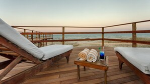 Une terrasse en bois avec deux chaises longues et une petite table sur laquelle sont posées des serviettes et une boisson.