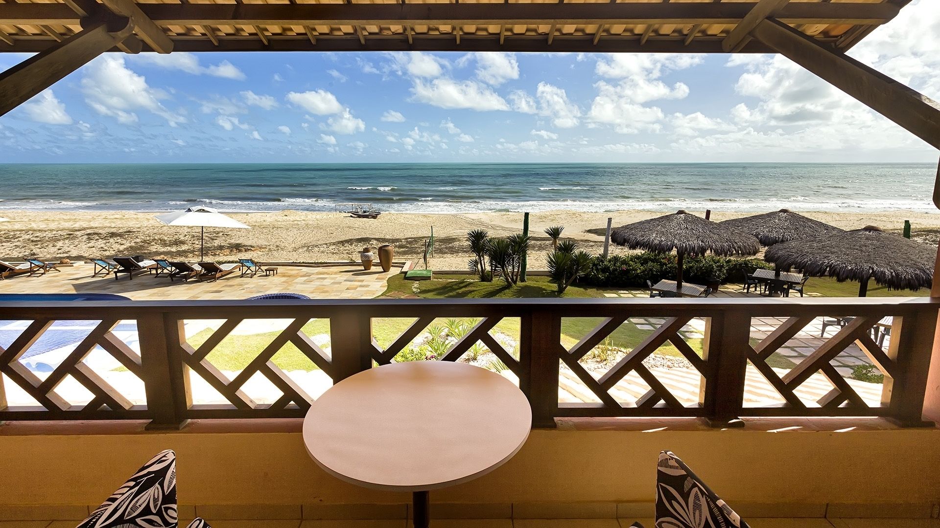 Vista de la playa desde un espacio cubierto con una mesa, sillas, sombrillas y sillones reclinables.