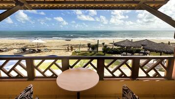 Vista de la playa desde un espacio cubierto con una mesa, sillas, sombrillas y sillones reclinables.