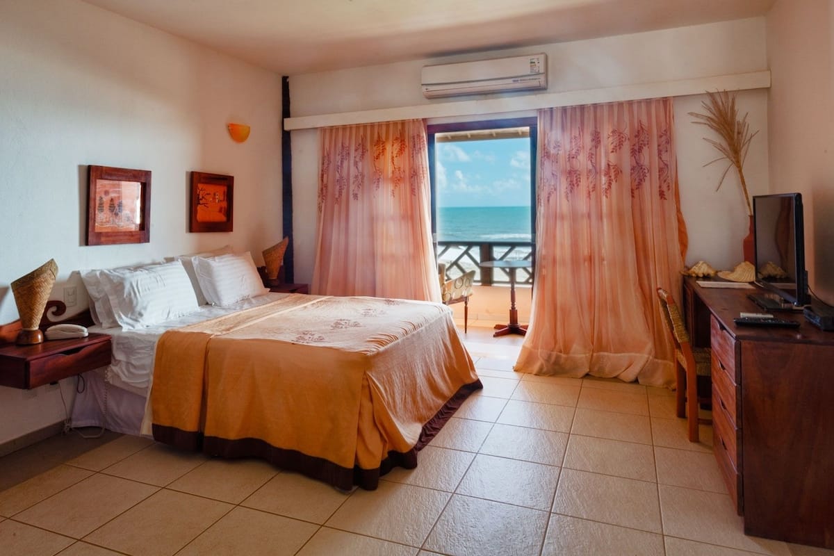 Een hotelkamer met een bed, een bureau, een televisie en uitzicht op de oceaan.