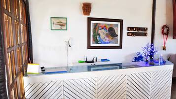 Una recepción con mostrador de vidrio, un cuadro enmarcado encima, un teléfono fijo en la pared y una corona decorativa.