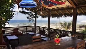 Un espace extérieur abrité, avec des tables et des chaises en bois, donnant sur la plage.