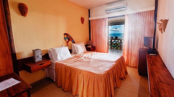 Habitación de hotel con cama, escritorio, silla, televisor y balcón con vista al mar.