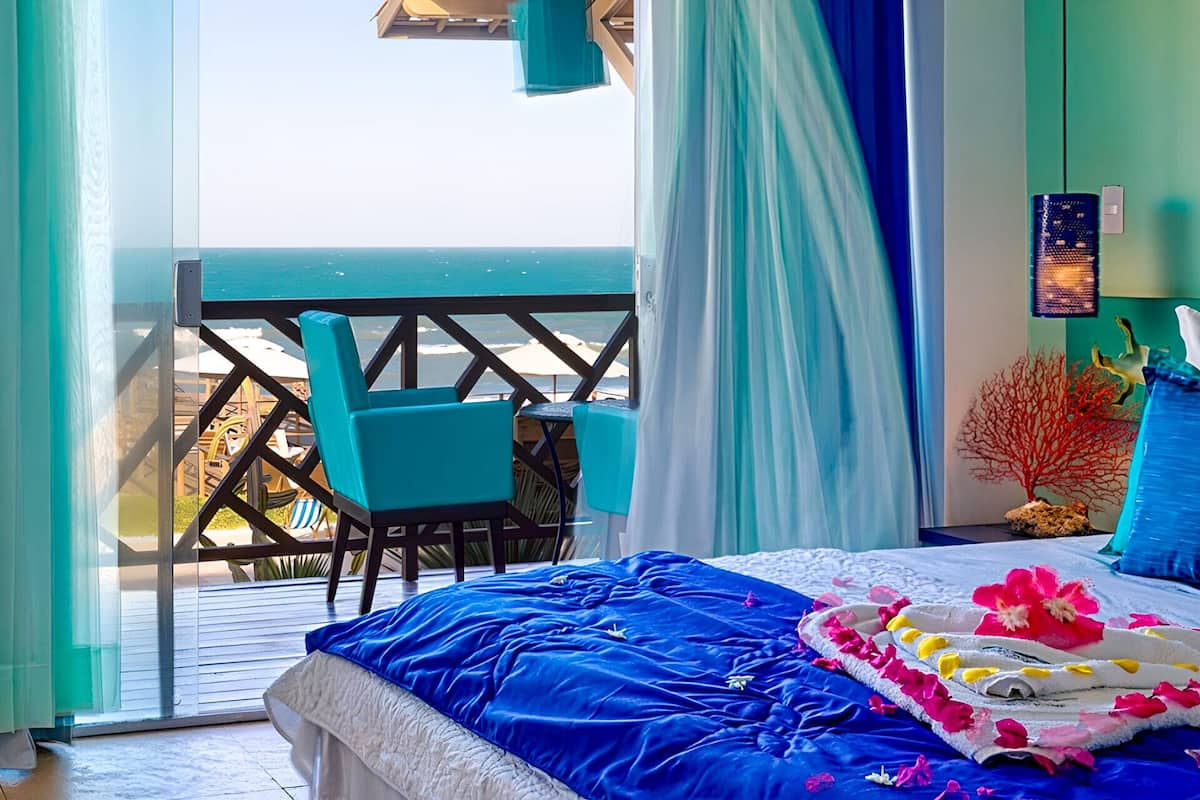 Een balkon met uitzicht op zee, een bed met een blauwe spreidek en een stoel.