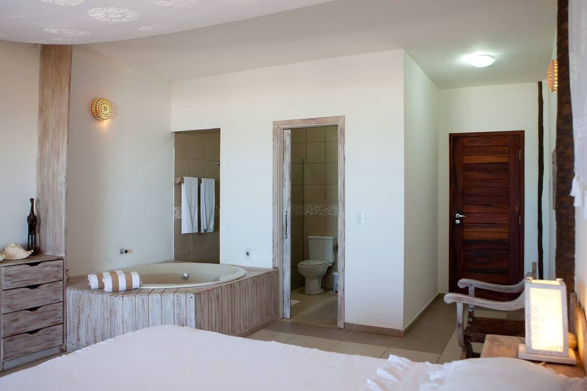 Een slaapkamer met een groot bed, een houten dressoir, een badkamer met een bad en een houten deur.