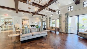 A spacious living room with a large sofa, a coffee table, and a dining area. There is a kitchen visible in the background.